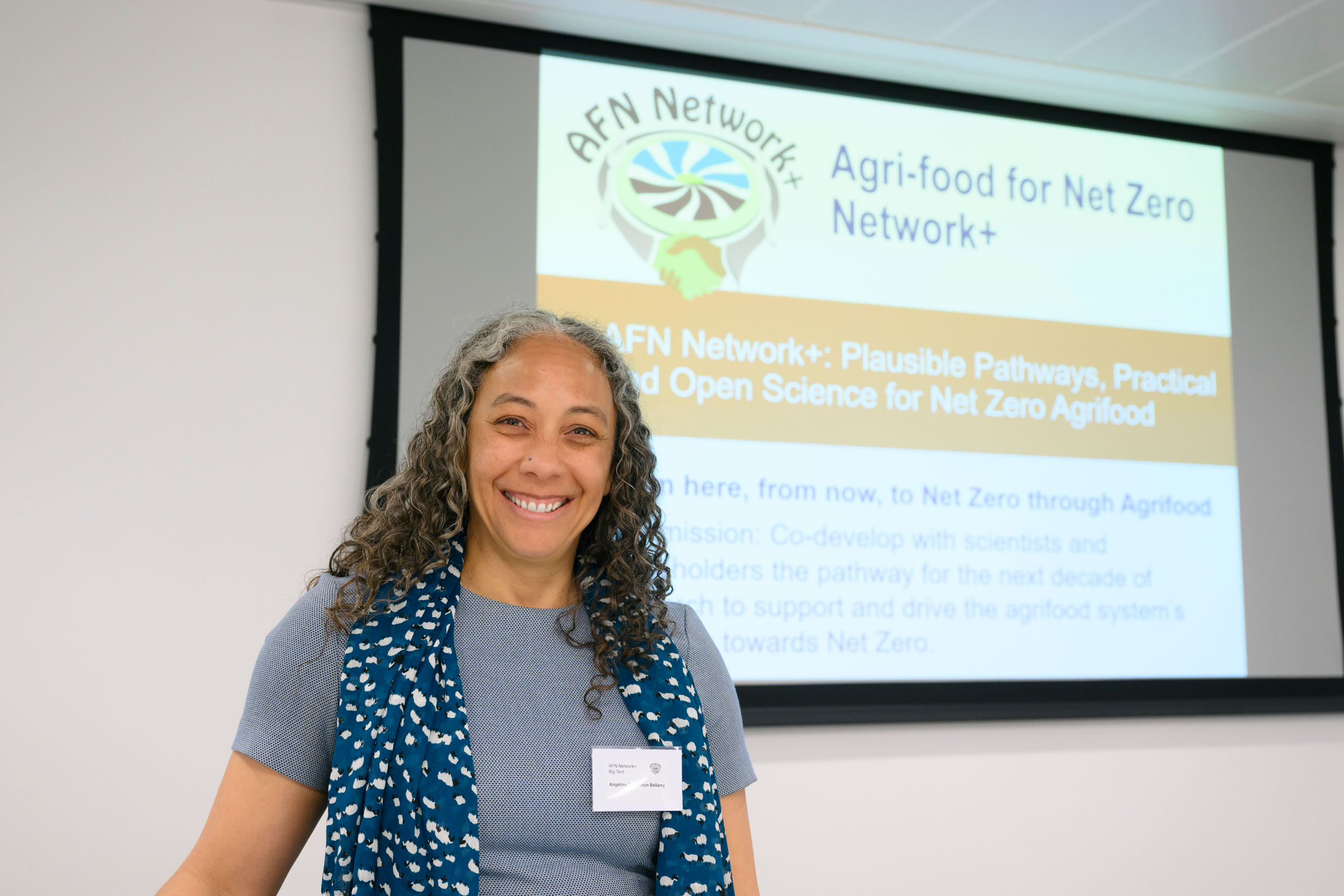 A person stood at the front of the room, smiling, ready to present at the AFN Network+ “Big Tent Event”